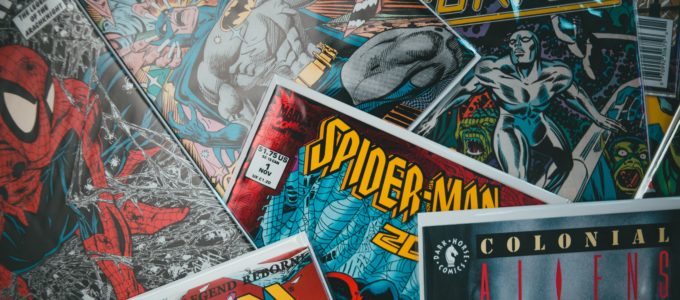 A variety of comic books issues in plastic sleeves strewn about. A Spider-man issue is at the center but Silver Surfer, X-Men, and Colonial Aliens are also visible.