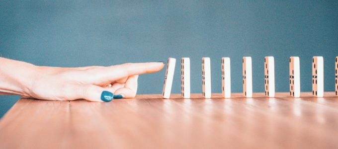 A woman pushes the first in a series of standing dominos arranged end to end in a row.